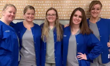 Five Herzing nursing students in blue scrubs smiling